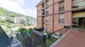 A multi-story residential building with balconies, a small garden area, and a view of a hillside.
