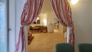Ein Zimmer mit großem Fenster, einem Esstisch und Blick in einen Wohnbereich mit Sofa und Küche.