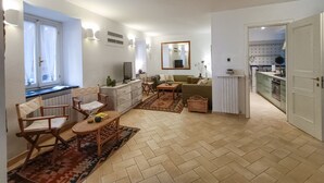 Ein geräumiger Wohnbereich mit einer Couch, einem Couchtisch und einem Esstisch. Durch eine offene Tür ist eine Küche zu sehen.