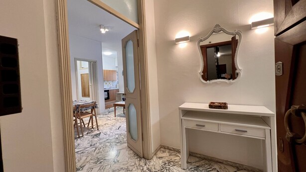 A hallway with a marble floor, a white console desk, and a mirror with wall sconces.