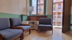 Ein Zimmer mit zwei grauen Polsterstühlen, einem kleinen Holztisch und einem Fenster mit Blick auf Gebäude.