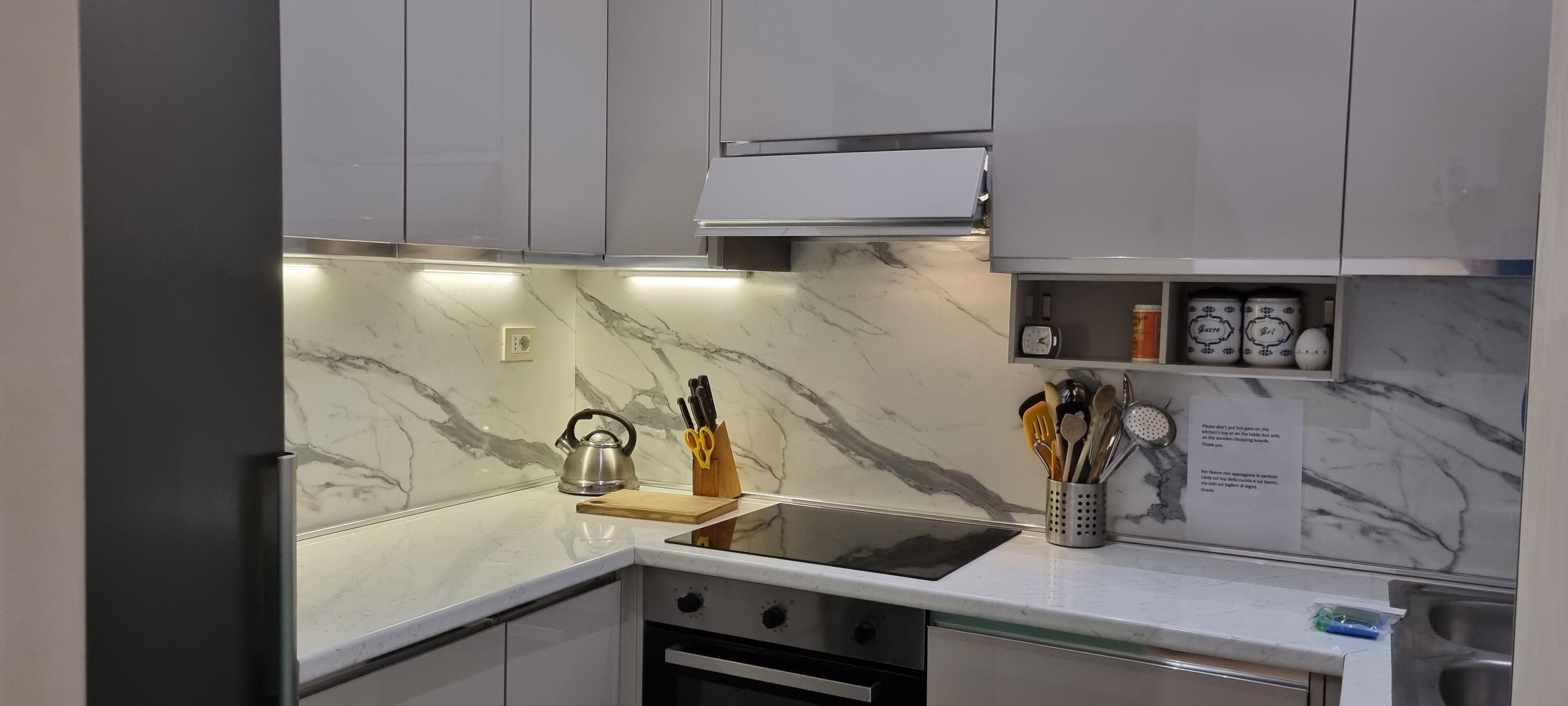 Una cocina moderna con encimeras de mármol, un hervidor, un bloque de cuchillos y una nota en la pared.