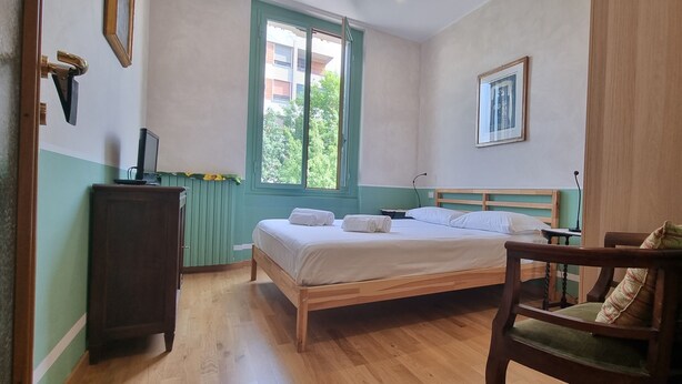 Ein Schlafzimmer mit einem hölzernen Bett, einem Holzstuhl, einem Schreibtisch, einem Fenster und einer Heizung.
