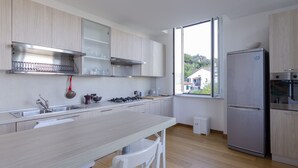 Eine moderne Küche mit hellen Holzschränken, Edelstahlgeräten und einem großen Fenster mit Blick nach draußen.
