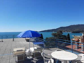 A terrace with outdoor seating, a blue umbrella, and a view of the sea and hills. - JOIVY Enjoy The Silence (Rapallo)