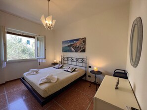 A bedroom with a bed, bedside tables, a nightstand, a wall-mounted mirror, and a painting.