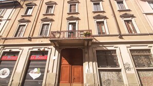 Ein Gebäude mit einem zentralen Eingang, mehreren Fenstern und einem Balkon mit Geländern.