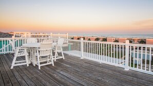 Um deck de madeira com mesa e cadeiras, com vista para uma praia e oceano.