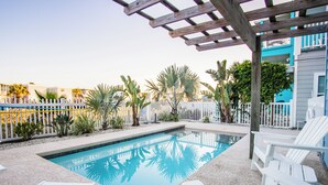Uma piscina com espreguiçadeiras brancas e uma pérgula de madeira.