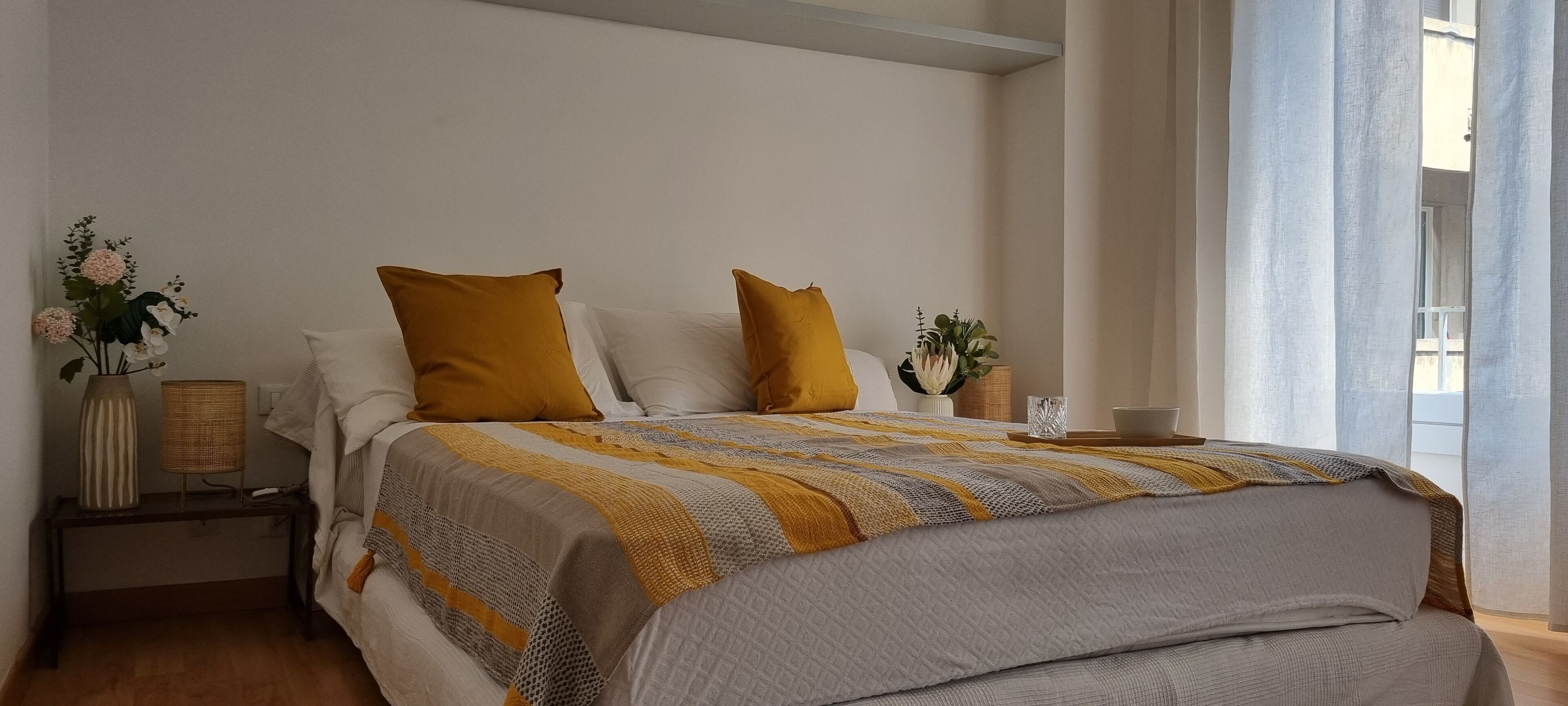Un lit bien fait, avec une couverture à rayures, deux oreillers et une table de chevet sur laquelle est posé un vase de fleurs.