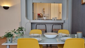 Un comedor con una mesa de vidrio, sillas amarillas, un tazón blanco y un espejo sobre la mesa.