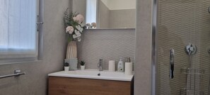 Ein Badezimmer mit weißem Waschbecken, einem Spiegel, einer Blumenvase und Pflegeprodukten.