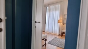 Una habitación de hotel con piso de madera, una cama blanca, una mesita y una lámpara.