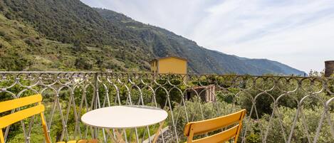 A balcony with yellow chairs and a table, overlooking a mountainous landscape.