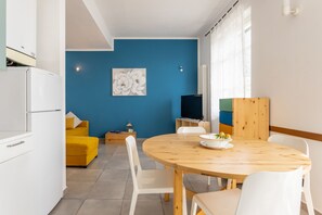 Eine moderne Küche mit weißen Schränken, einem gelben Sofa und einem Essbereich mit Holztisch und Stühlen.