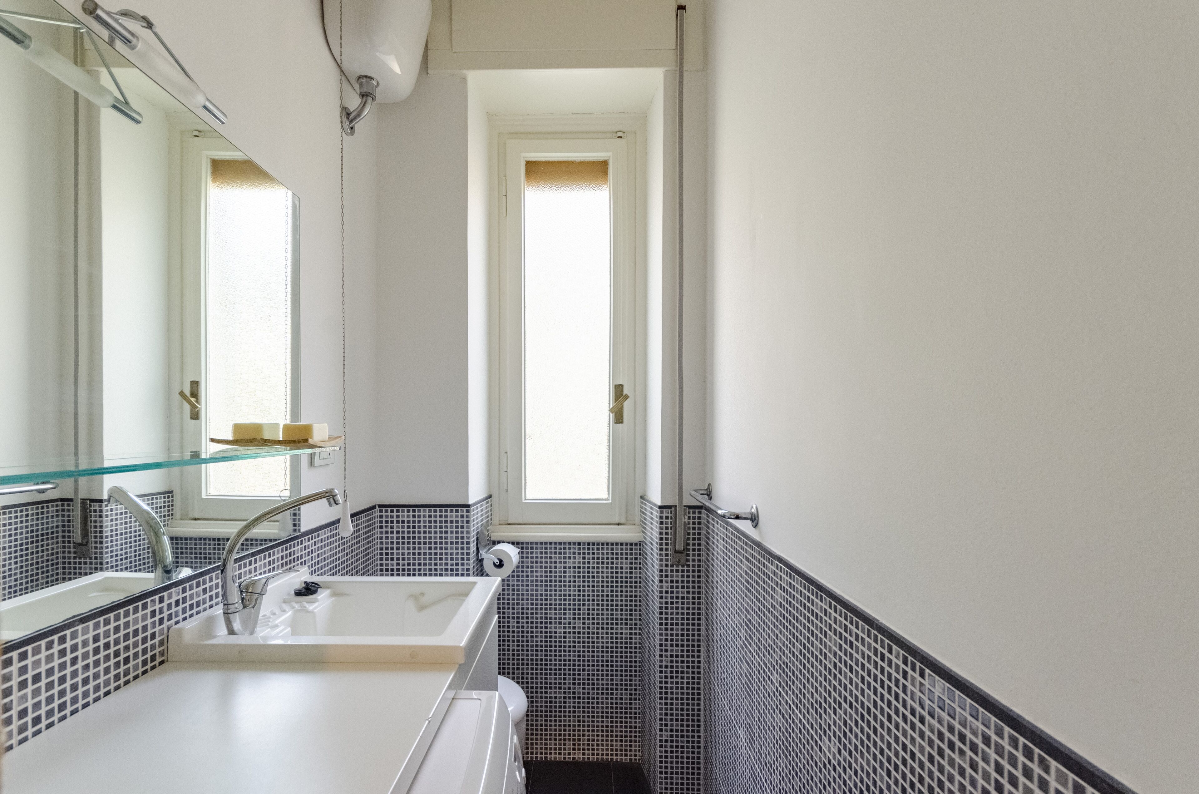 A bathroom with a white sink, a glass shelf with toiletries, and a window providing natural light.