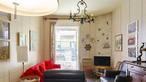 Una sala de estar con un sofá rojo, un sofá de cuero negro, sillas de mimbre, un televisor y un mueble de madera.