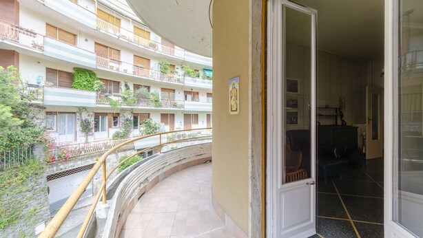 Un edificio residencial de varios pisos con balcones, un balcón curvo con barandilla amarilla y una puerta que da a un espacio interior con piso oscuro.