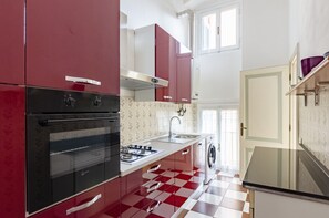 A kitchen with red cabinets, a gas stove, a sink, and a washing machine.