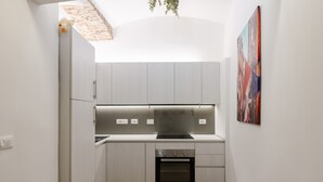 Eine kompakte Küche mit Backofen, einem kleinen Mülleimer und einem Essbereich mit einem Stuhl.