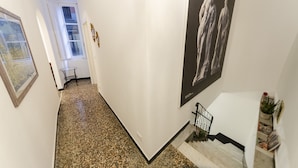 Ein Korridor mit Granitboden, weißen Wänden und einer Treppe mit schwarzer Geländer.