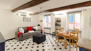 A living room with a sofa, ottoman, dining table, chairs, and a ceiling fan. - JOIVY Flat By The Sea Promenade (Camogli)