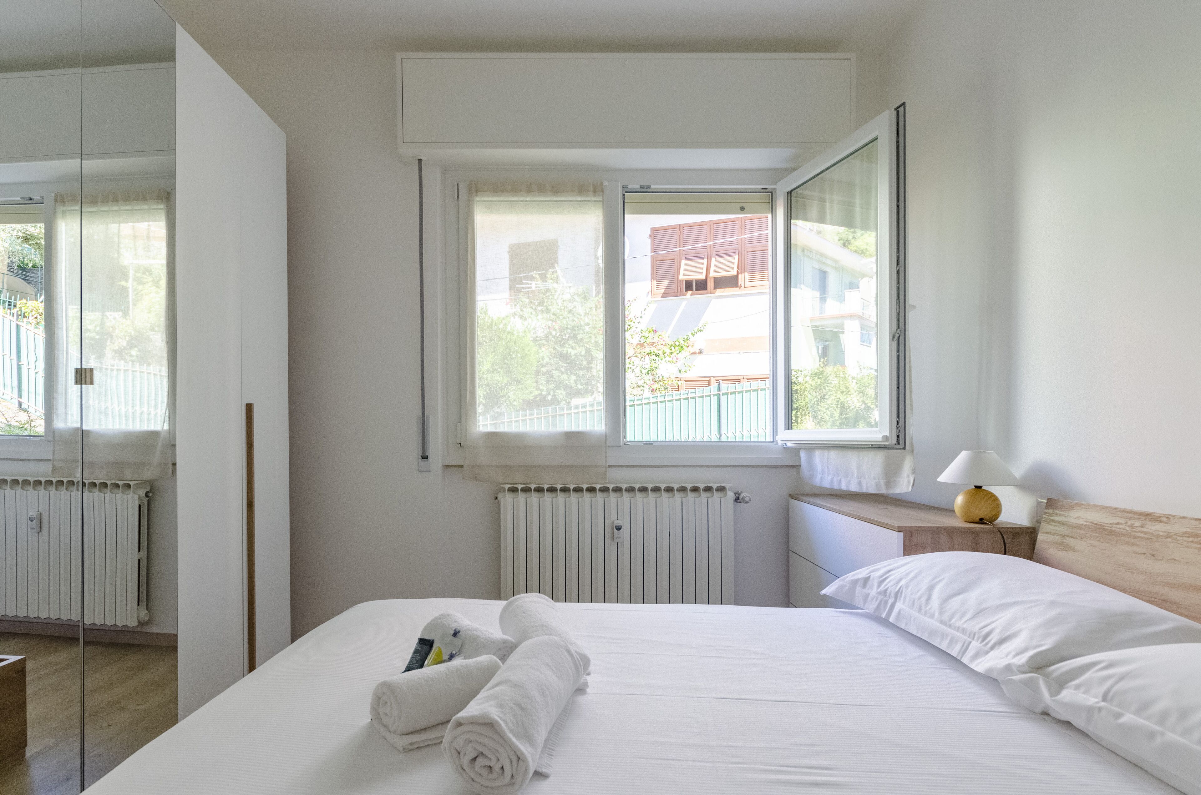 Une chambre d’hôtel avec un grand lit, une fenêtre donnant sur des immeubles, une table de chevet avec une lampe et un radiateur.