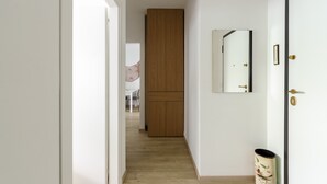 A narrow hallway with a wooden wardrobe, a mirror, and a trash can.