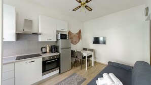 A compact kitchen with a microwave, stove, and refrigerator, a dining area with a table and chairs, and a gray sofa with towels.