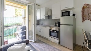 A compact kitchen with white cabinets, a microwave, a coffee maker, and an oven. There is a sliding glass door leading to an outdoor seating area with a table and chairs.