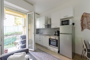A compact kitchen with white cabinets, a microwave, a coffee maker, and an oven. There is a sliding glass door leading to an outdoor seating area with a table and chairs.