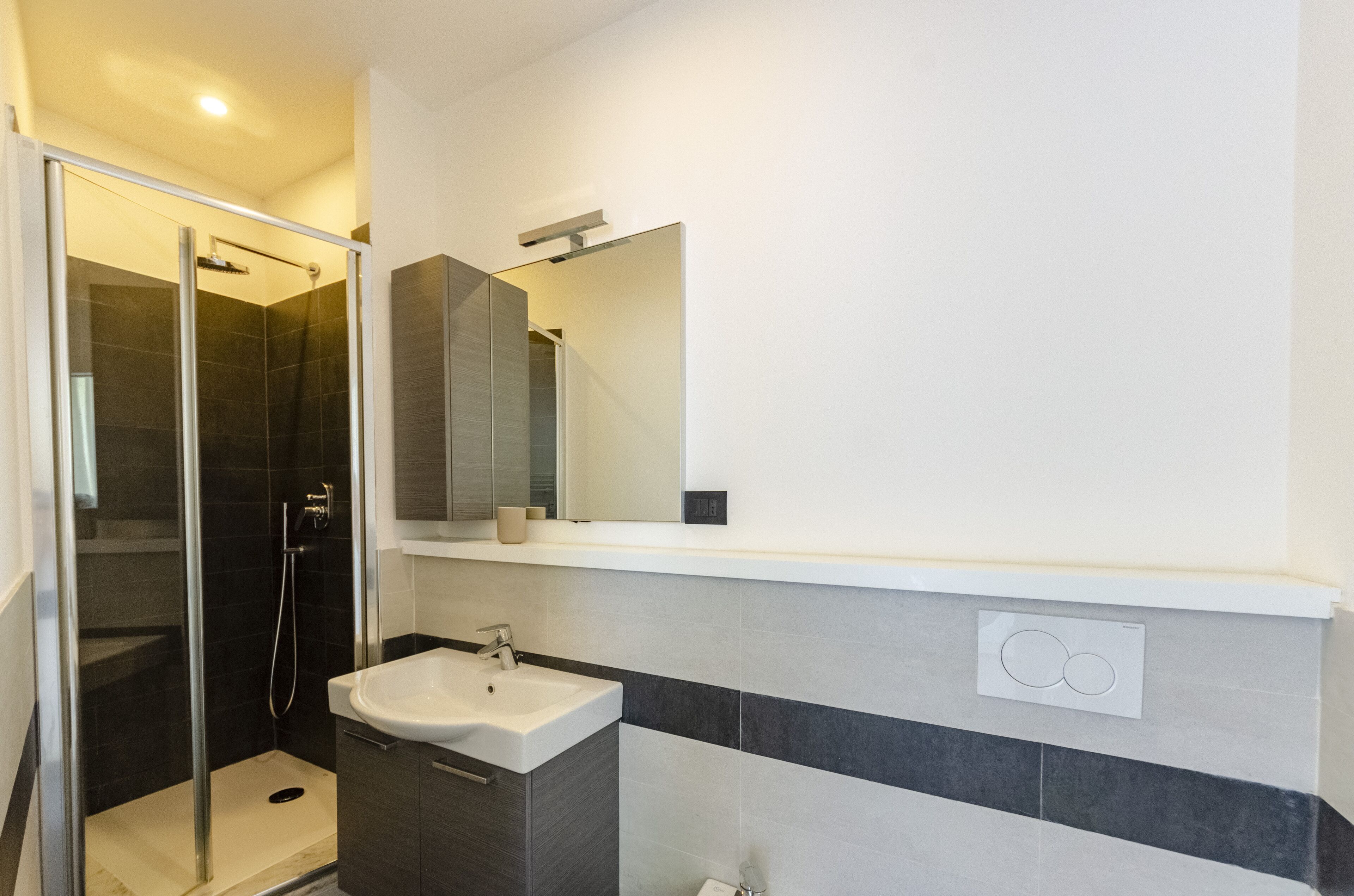 A modern bathroom with a glass-enclosed shower, a white sink, and a large mirror.