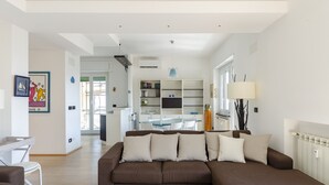 A modern living room with a brown sectional sofa, a dining table with chairs, a kitchen area, and a large window. - JOIVY Great Flat W/Sea View (Genoa)