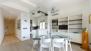 A modern kitchen with white cabinets, a glass dining table, and a blue pendant light. - JOIVY Great Flat W/Sea View (Genoa)