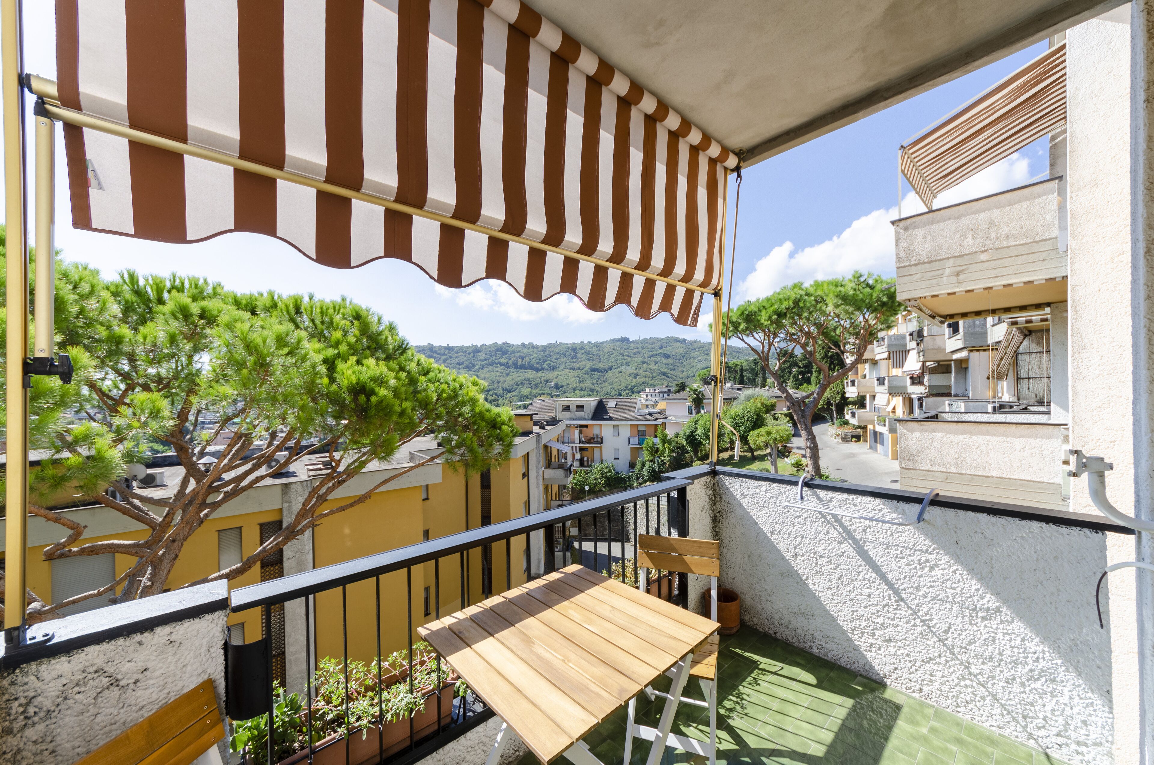 Un balcone con un tenda a righe, un tavolo in legno e piante in vaso.