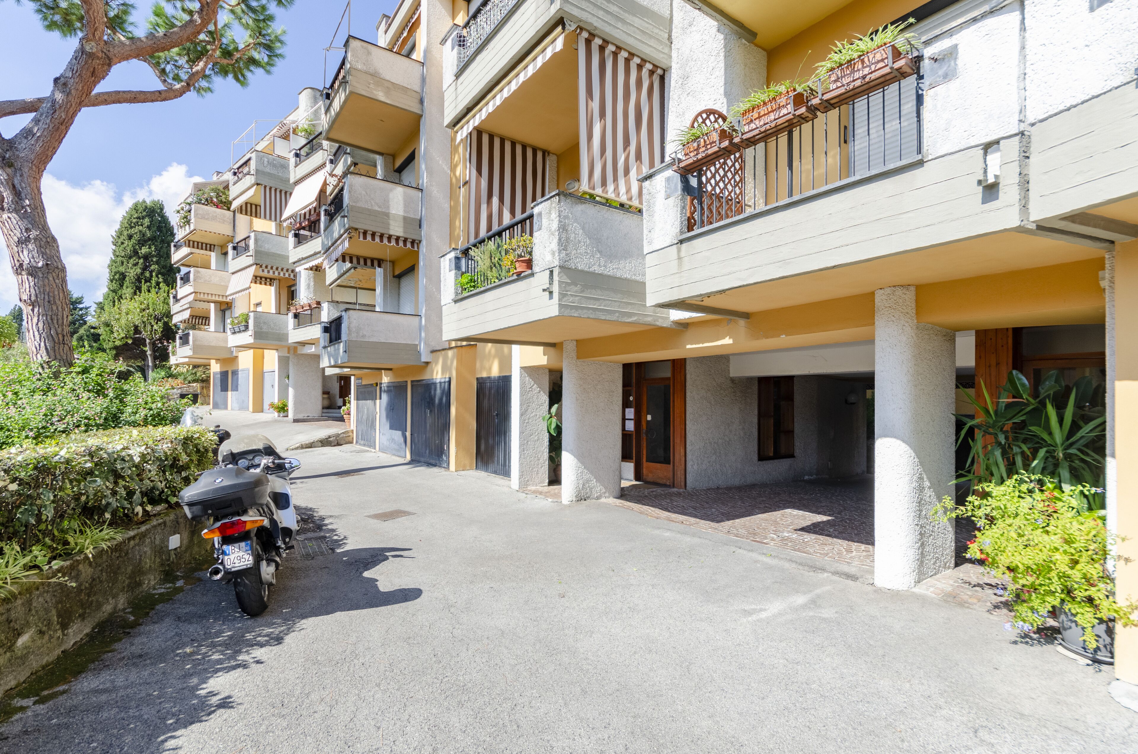 A multi-story hotel with balconies, a parked motorcycle, and a well-maintained garden.