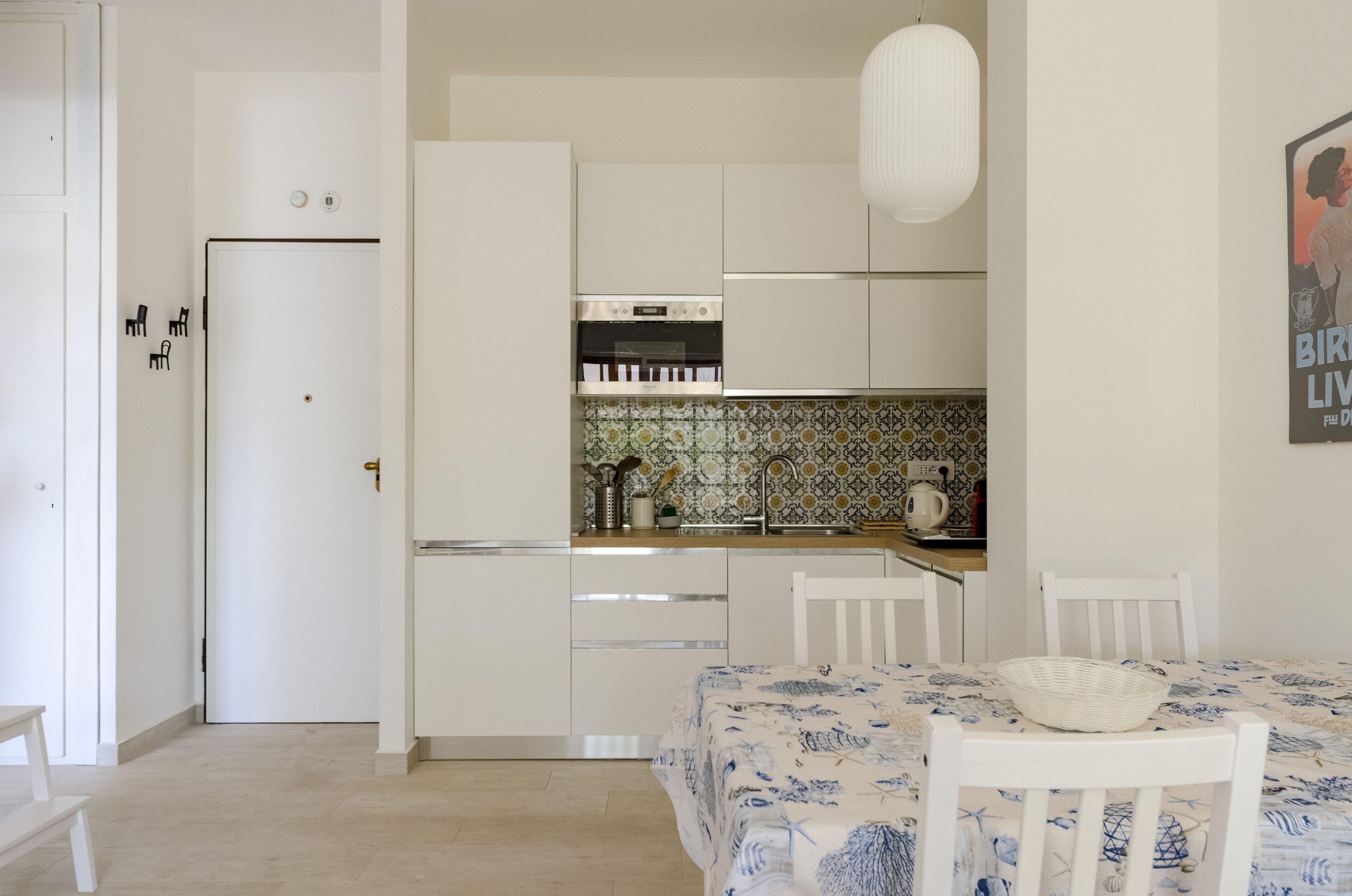Una cocina compacta con armarios blancos, horno integrado y salpicadero de azulejos.