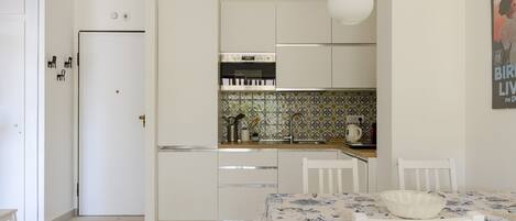 Una cocina compacta con armarios blancos, horno integrado y salpicadero de azulejos.