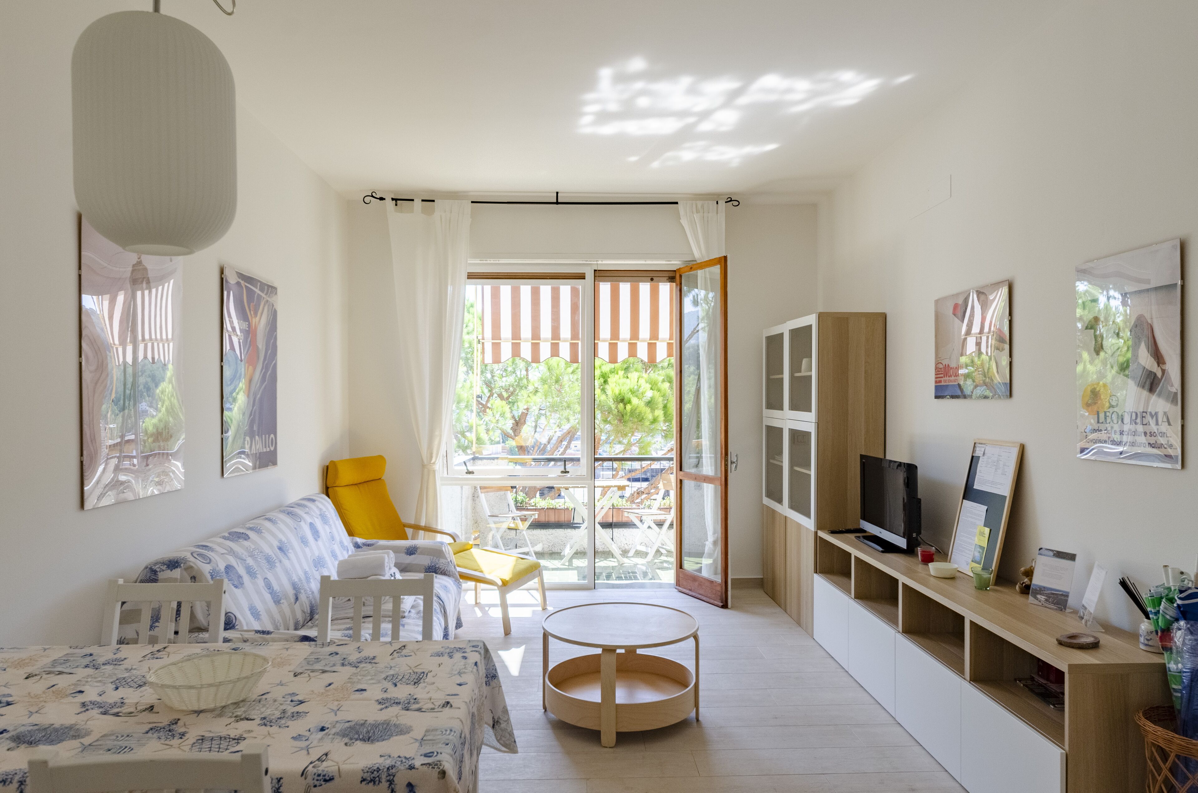 A bright room with a sofa, chairs, a table, a TV, and a view through a glass door.