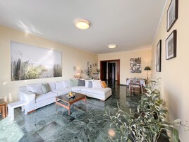 A spacious living room with a white sectional sofa, a coffee table, and a dining area with a table and chairs.