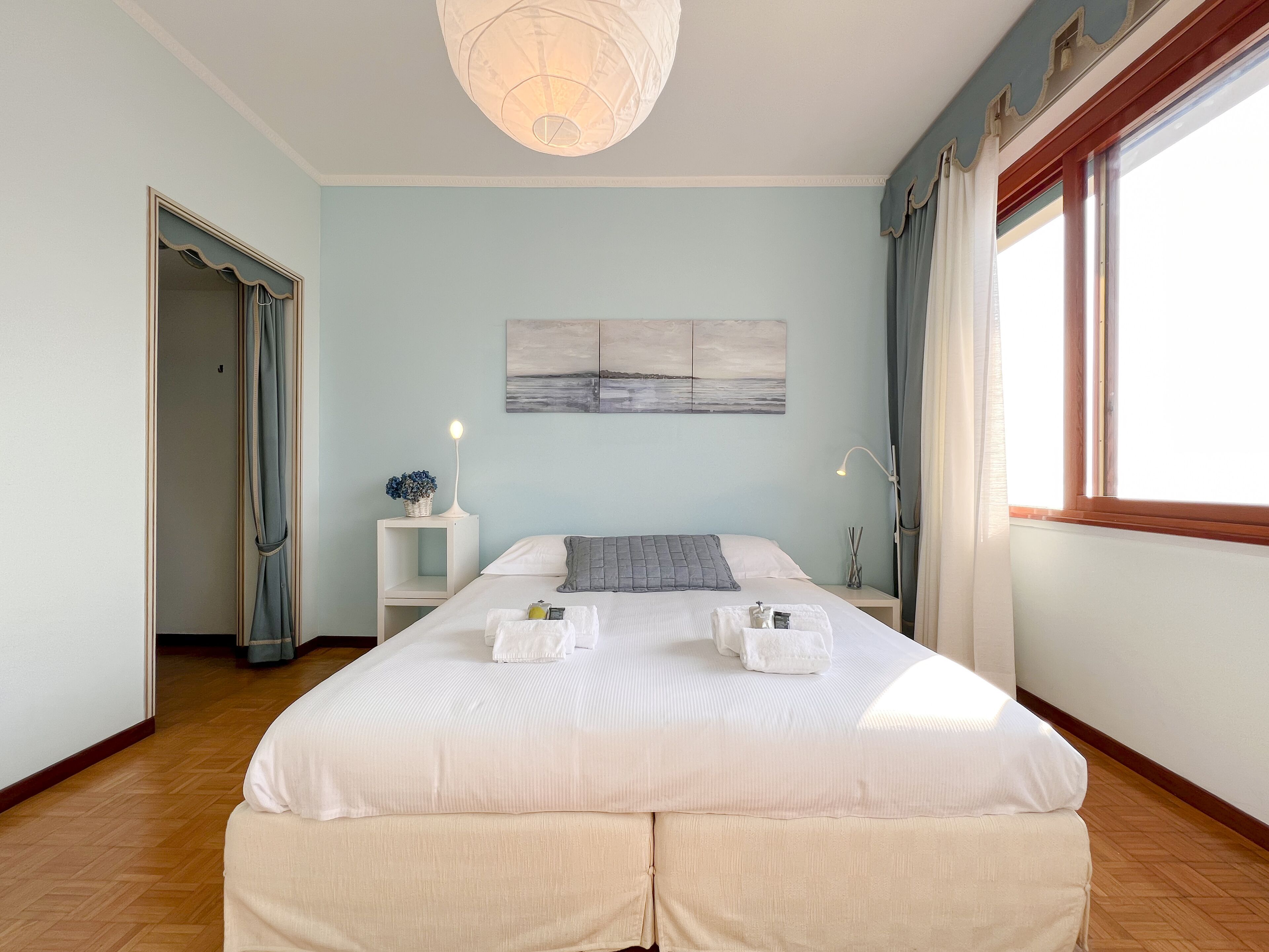 A bedroom with a large bed, bedside tables, a wall-mounted artwork, and a window with curtains.