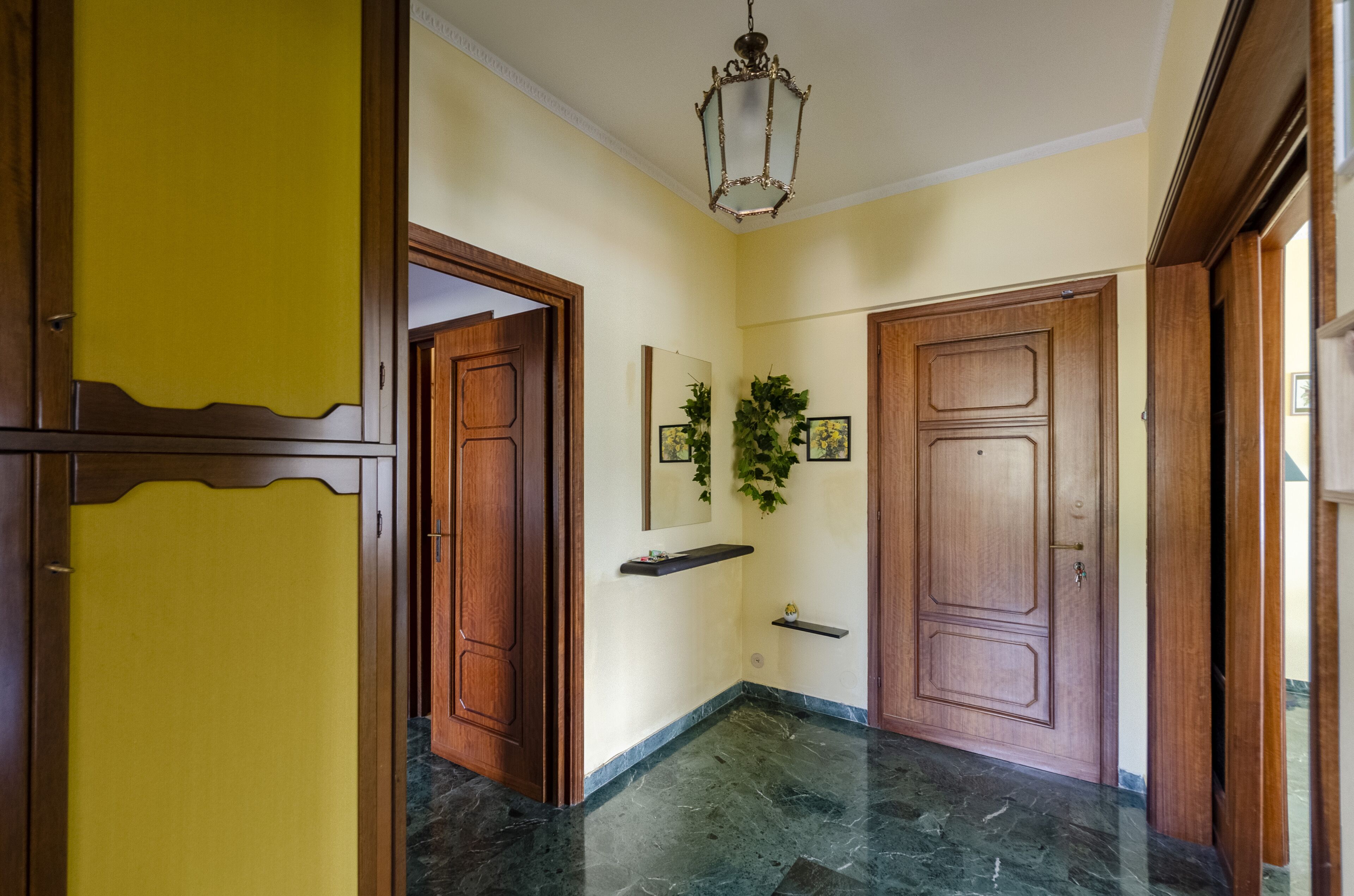 Un corridoio con pavimento in marmo, porte in legno e un lampadario.