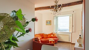 En stue med en rød sofa, en hvid stol, en glaskrukke med grønne planter og en lysekrone.