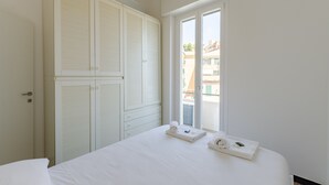 A bedroom with a large wardrobe, a bed with white linens, and a window with a view of buildings. - JOIVY Two Steps From The Sea In Genoa (Genoa)