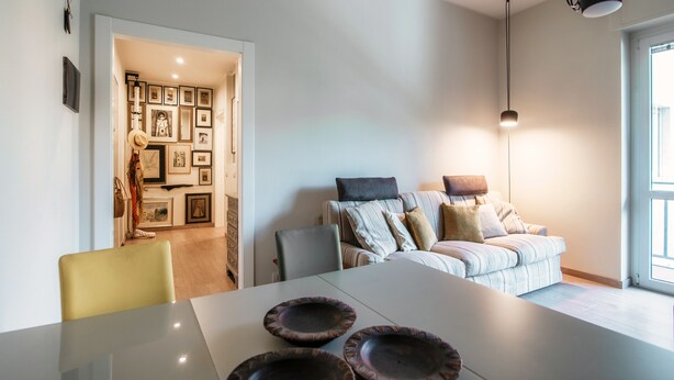 Un salon moderne avec un canapé, une table à manger avec de l’assiette, et un couloir orné de tableaux encadrés.