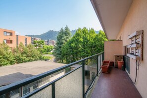 Un balcon avec vue sur les immeubles et les arbres, un sol carrelé et du mobilier d’extérieur.