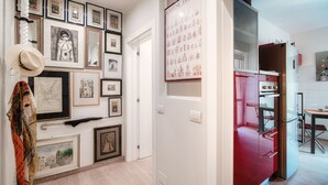 Un couloir orné de tableaux encadrés, une porte donnant sur une cuisine où se trouve un réfrigérateur rouge.