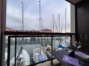 Un balcon donnant sur un port de plaisance, une table avec une bouteille de vin et un verre.