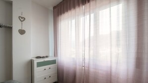 A bedroom with a bed, a dresser with drawers, a window with sheer curtains, and two heart-shaped decorations on the wall. - JOIVY Family Flat W/Balcony (Como)