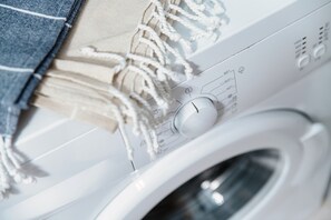 Une machine à laver blanche, dotée d’un panneau de commande, et un morceau de tissu en denim qui pend à proximité.